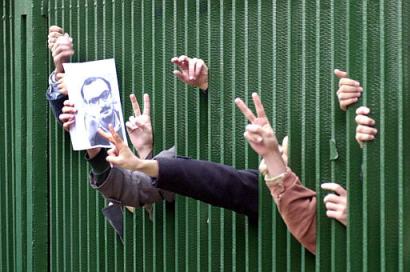 Iranian students chant 'referendum' and flash the victory sign to police as they hold a photo of Hashem Aghajari, who has been sentenced to death for insulting Islam, during a demonstration  entitled: 'The anti-dictatorship gathering of students' behind the main entrance of Tehran University Saturday Dec. 7, 2002. Thousands of students called for a nation-wide referendum to get Iran out of a political deadlock where unelected hard-liners have used the courts they control as a political instrument to stall voted presidential reforms. (AP Photo/Hasan Sarbakhshian)